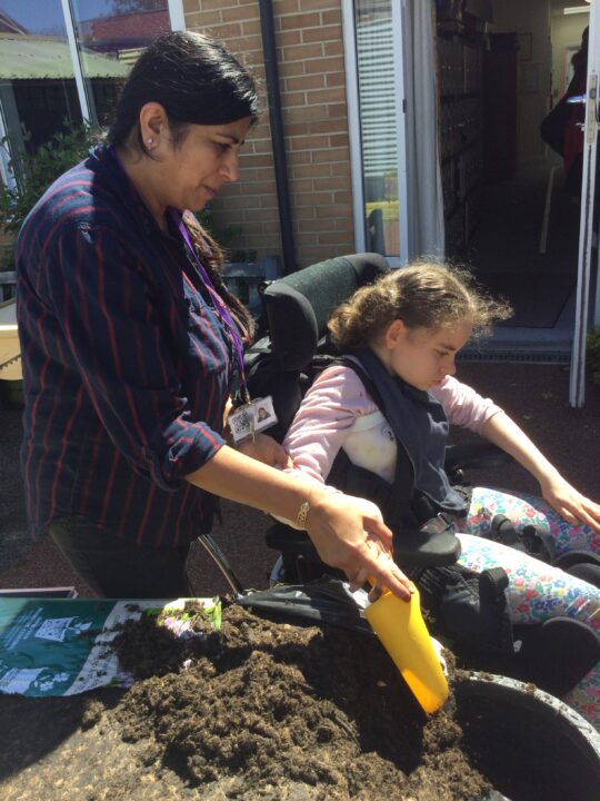 Photo of a girl with a neurodisability and a specialist learning support assistant outside at Pace school in a gardening lesson digging some soil.