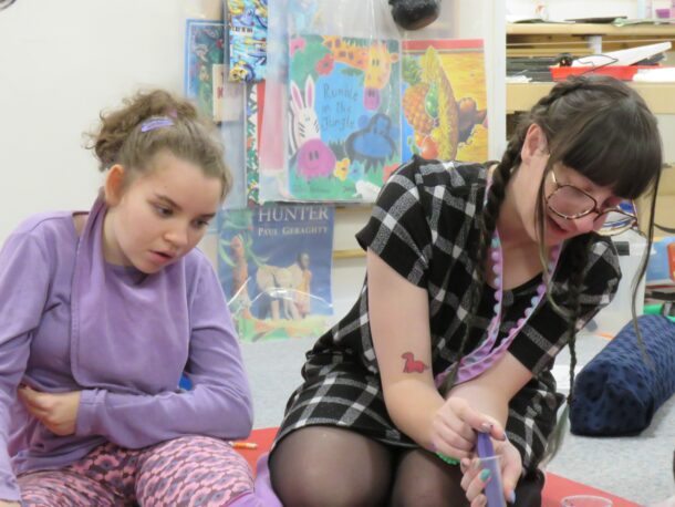 One of our students, dressed in purple for Rett Syndrome Awareness Month, watches as a Learning Support Assistant uses a syringe to decorate a biscuit with purple icing.