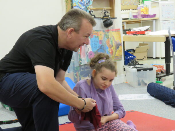 One our the learning support assistants kneels next to a Pace student as he washes her hands clean with a wet flannel.