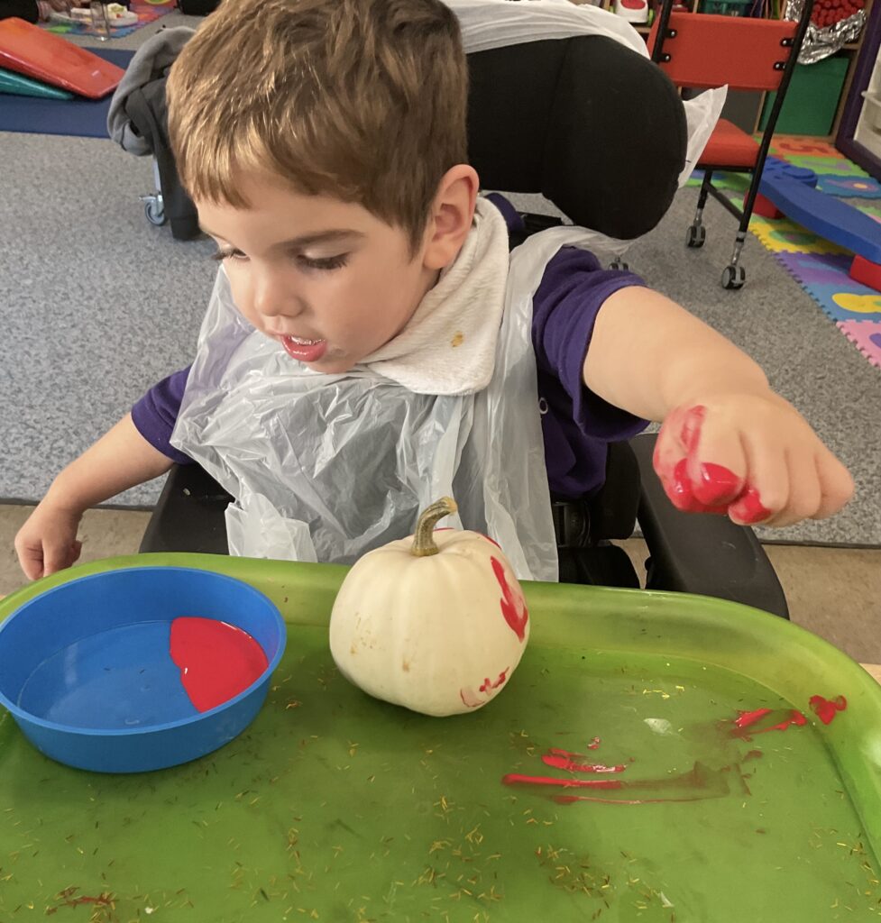 A Pace student paints a small white pumpkin with red paint.